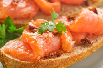 Sandwiches with salted salmon. Open sandwiches from cereal or whole grain rye bread with salted salmon, sesame seeds and dried tomato on white marble stand. Seafood. Healthy food. Scandinavian cuisine