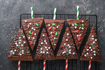 Chocolate brownies Christmas tree with chocolate icing and festive sprinkles on stone table. Christmas food ideas sweet homemade Christmas holidays pastry concept. Holiday cooking concept. Top view.