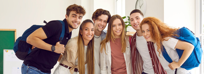 Group portrait of happy and positive male and female university students in classroom. Six smart international students in casual clothes smiling together and looking at camera. Panorama. Web banner.