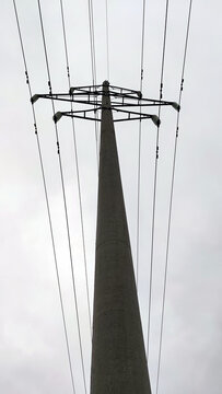 A tall concrete pole with electrical wires. A cement pylon of a power line under a light gray sky that is covered with clouds. Oprah is holding several high voltage metal wires.