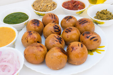 Litti in white plate with tomato, brinjal, potato, pointed gaurd and coriander chutney or chokha and ghee. It is popular in Bihar, Uttar Pradesh and Jharkhand. White background