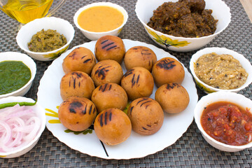 Litti Chokha in white plate with chicken, tomato, brinjal, potato, pointed gaurd and coriander chutney or chokha and ghee. It is popular in Bihar, Uttar Pradesh and Jharkhand.