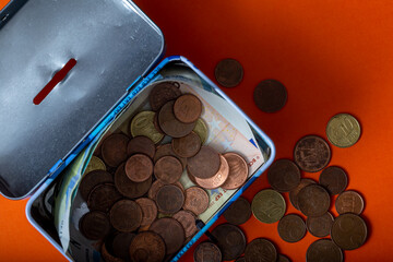 Money box with coins and banknotes on orange background