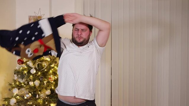 Christmas holiday party at home, caucasian drunk male dancing in the living room performing a strip tease throwing away his Xmas jumper, slow motion