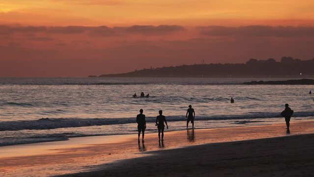 Silhouettes of people walking on sandy beach and surfers at the sunset background on the Atlantic coast of Portugal.