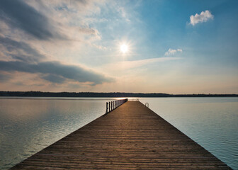 Naklejka na ściany i meble Late afternoon over a pier. Blue and orange sky over a lake. Late afternoon over a lake side.