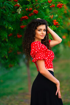 Pretty brunette curly girl in red gipsy costume and accessories posing on nature with rowanberry and green background. 