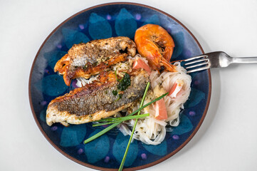 Fried sea bream fillet and shrimp with glass noodle on blue decorative plate on white.