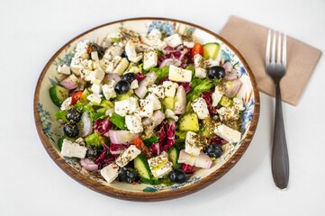 Greek salad on big decorative plate, fork, napkin.