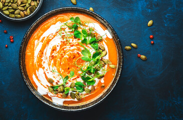 Spicy vegan pumpkin soup with pumpkin seeds, coconut cream and pea sprouts. Winter or autumn healthy vegetarian food. Soup bowl on blue table background. Top view