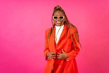 Black ethnic woman with braids on a pink background, portrait in a red suit and yellow pants smiling