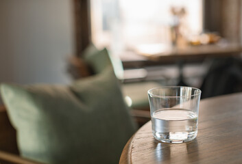 Closeup of a glass of water on wooden table in modern interior. Unrecognizable interior. Cafe or restaurant interior concept. Copy space.