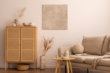 Warm and cozy interior of living room space with mock up poster frame, round table, rattan commode, vase with dried flowers and walking young woman. Minimalist home decor. Template.