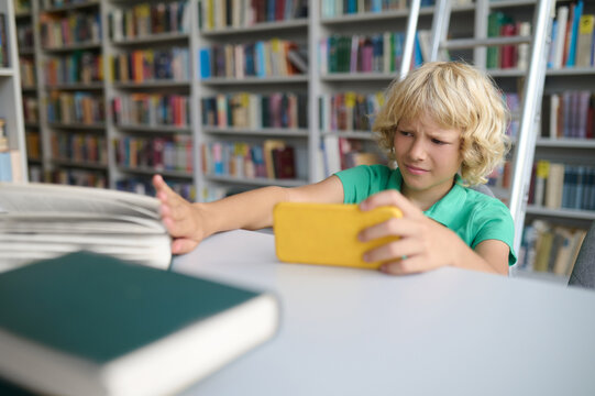 Blonde boy sitting in the library and spanding time online