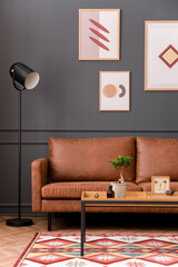Aesthetic interior of living room with mock up poster frame, brown sofa, wooden coffee table, black lamp, patterned rug, gray wall, plants in flowerpot and personal accessories. Home decor. Template..