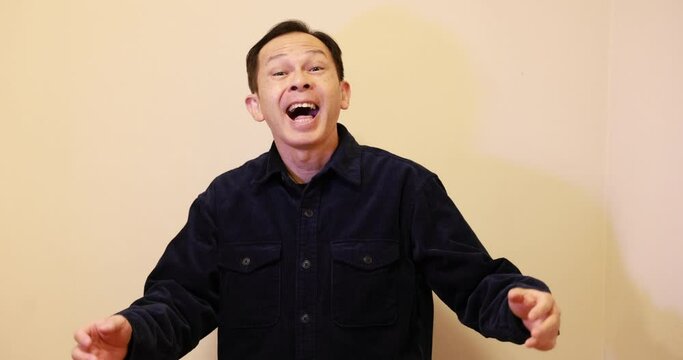 Laughing middle-aged Japanese man in navy blue casual shirt. Conceptual image of world peace, stability in daily life, and sustainable living. Slow motion 4K video.