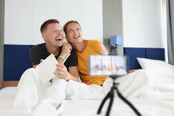 Happy smiling couple recording video in bed on smartphone
