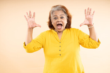 Shouting senior old indian woman standing isolated over beige studio background.
