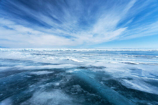 Unusual winter landscape of frozen Baikal Lake on February day. Above icy endless desert, beautiful stratus clouds adorn the blue sky. Natural cold background. Winter travel and outdoor recreation