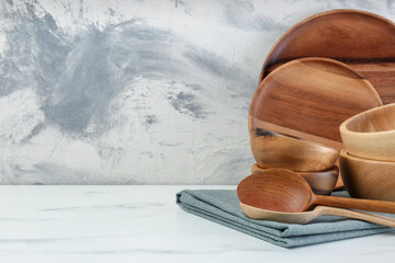 Set of wooden tableware on white marble table against textured wall. Space for text