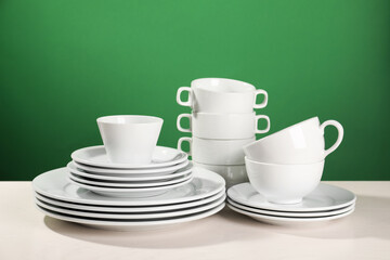 Set of clean dishware on white table against green background