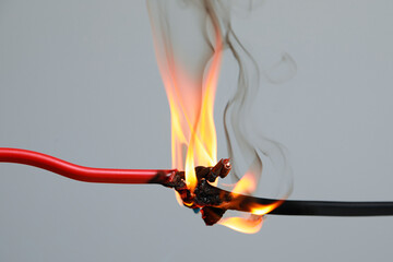 Inflamed red wire on grey background, closeup. Electrical short circuit