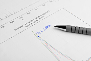 Paper with printed scatterplot graph, written mathematical calculations and pen, closeup