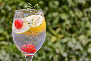 Delicious refreshing lemonade with raspberries against green blurred background, closeup. Space for text