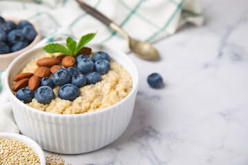 Bowl of delicious cooked quinoa with almonds and blueberries on white marble table, space for text