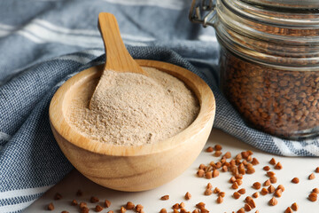 Bowl of buckwheat flour and glass jar with grains on white table, closeup