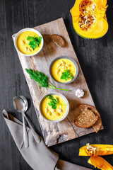 Vegetarian autumn pumpkin soup, seeds, creamy silky texture, cilantro parsley dill greens, croutons, bread, garlic on black table. Slavic Ukrainian Russian national traditional healthy vegan food
