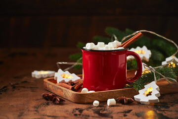 Red cup of hot cocoa with marshmallows on wooden table with christmas tree for christmas