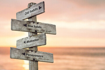 old habits new habits motivation perseverance text written on wooden signpost outdoors at the beach during sunset