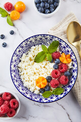Cottage cheese in bowl garnished with raspberries, blueberries, physalis and mint leaves on white background