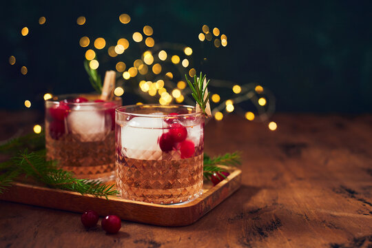 Alcoholic cocktail or non-alcoholic cocktail with vodka and cranberries with ice with fir branches and glowing garland for christmas on wooden background