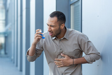 An attack of asthma, allergies. A young Hispanic, African American man is standing outside using an...