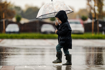 A cute little boy is walking on the street with his umbrella on a rainy weather.