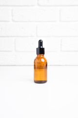 One amber bottle with a pipette on a white table, selfcare cosmetic products. Front view