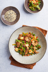 Wok with turkey meat, corn, green peas, green beans and carrots served on gray background with chopsticks. Asian food concept of street food