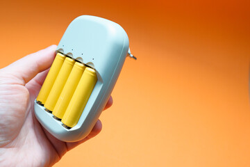 Charger and Batteries in man`s hand. Male hand holding charger with yellow AA batteries, on orange background
