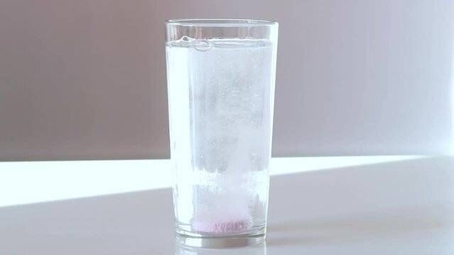 A woman throws an electrolyte tablet into the water. The pink electrolytes dissolve. Oral rehydration salts for athletes.