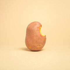 minimal creative cooking ccomposition of raw bitten potato on bright brown background.