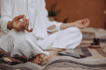 Crop woman with mudra hands sitting in Lotus pose and practicing yoga on bed at home 