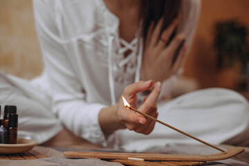 Unrecognizable woman burning incense stick during aromatherapy and yoga at home  - obrazy, fototapety, plakaty