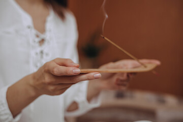 Crop unrecognizable woman burning incense stick with smoke and doing aromatherapy at home 