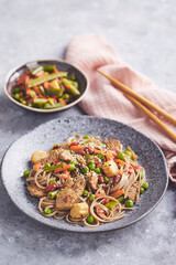 Wok with turkey meat, soba noodles, corn, green peas, green beans and carrots served on gray background with chopsticks. Asian food, concept of street food
