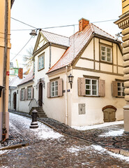 Beautiful narrow street in Riga Old Town with old houses, buildings and street lamps in winter covered by the snow, vertical 