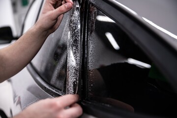 Employee of a car wash or a car detailing studio applies a colorless PPF protective film to the car...