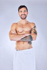 Fototapeta na wymiar Shower, towel and hygiene with a topless man in studio on a gray background for wellness or body care. Portrait, cleaning and tattoo with a handsome young male standing arms crossed in a bathroom