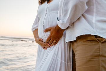 The man holds his pregnant wife's tummy and she holds her tummy too, the couple in love is walking along the small Praia de Paredes da Vitória, enjoying the freshness of the air and their love. 